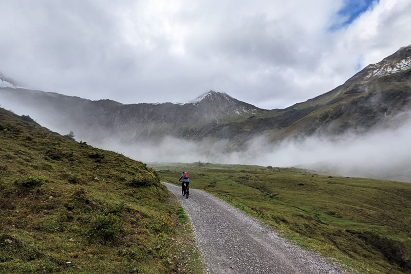 Privat Radfahrer auf schmaler Kiesstraße in Berglandschaft, Nebel zieht durch Hochtäler.