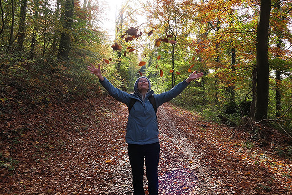 Privat Eine Person steht im Herbst im Wald. Die Person schmeißt Blätter in die Luft. Der Boden ist voller Laub.