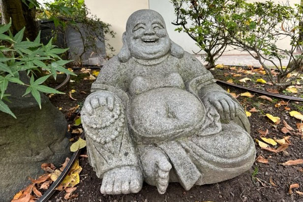 Privat Eine graue, sitzende Buddhastatue. Im Hintergrund Büsche.