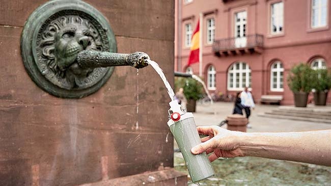 Hand füllt Trinkflasche an einem Trinkwasserspeier auf.