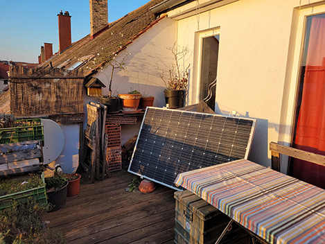 Solarmodul auf einem Balkon mit Pflanzen und gedecktem Tisch bei Sonnenuntergang