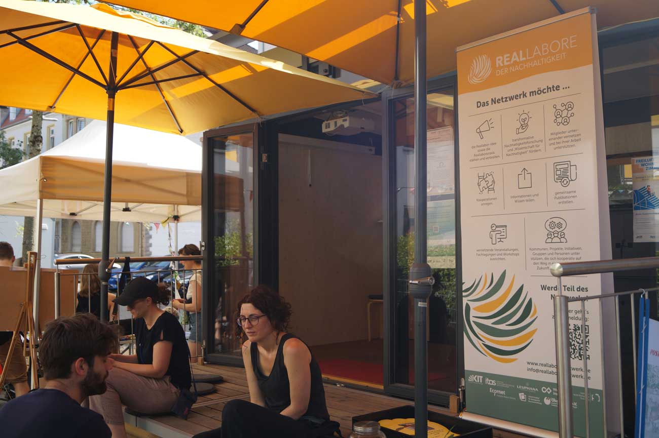 Menschen sitzen vor dem MobiLab in der Sonne.