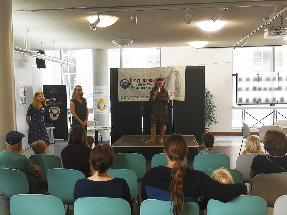 Publikum hört Vortrag von Franziska Poike auf einem Podium und Banner vom Klimamonster.