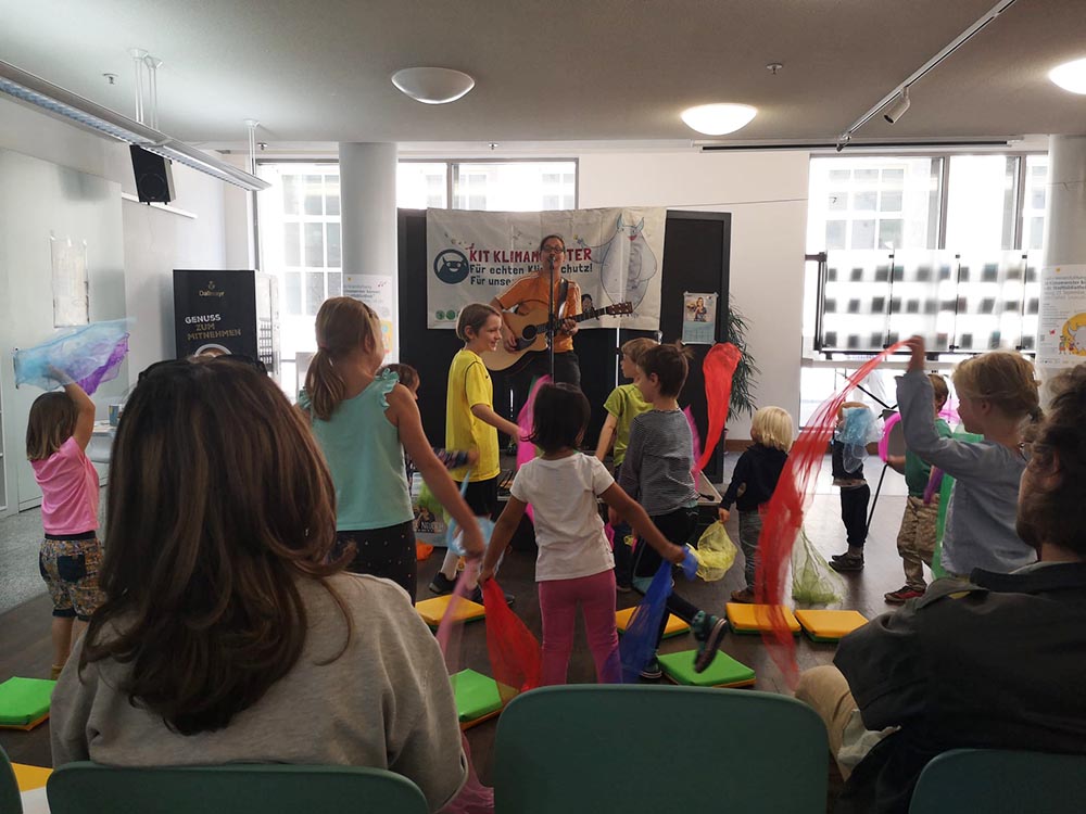 Kinder tanzen mit bunten Tüchern während einer musikalischen Veranstaltung.
