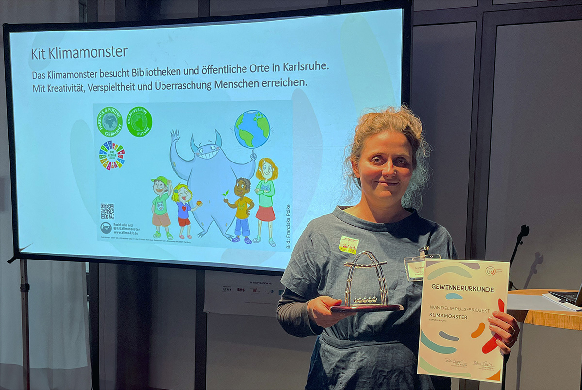 Franziska Poike hält Gewinnerurkunde und Trophäe zum Wandelimpuls-Projekt „Kit Klimamonster“ in Karlsruhe.