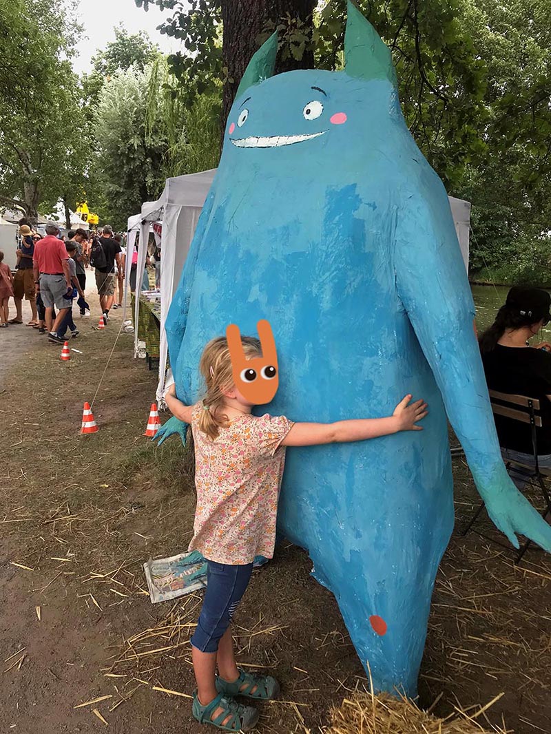 Mädchen umarmt blaue, freundliche Monster-Figur, Kit Klimamonster, beim Fest in Karlsruhe.
