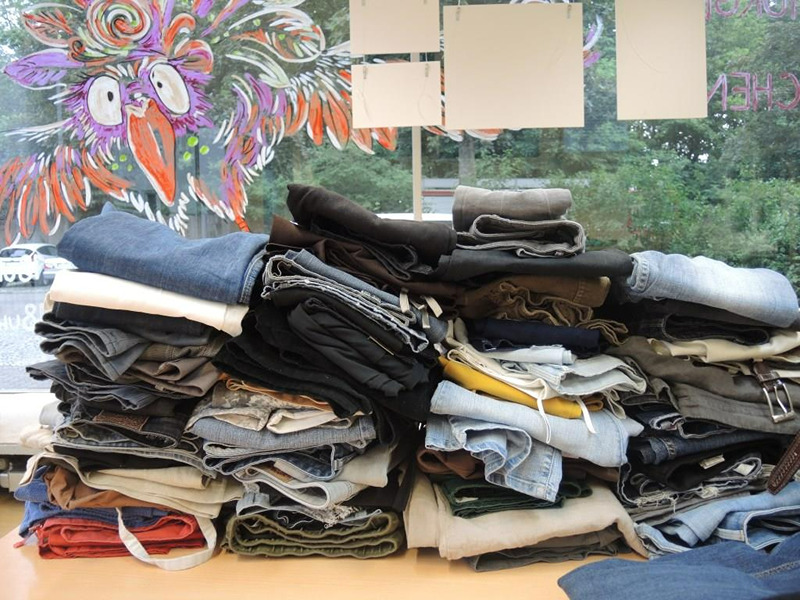 Gestapelte, gefaltete Jeans und Hosen beim Kleidertausch im Zukunftsraum.