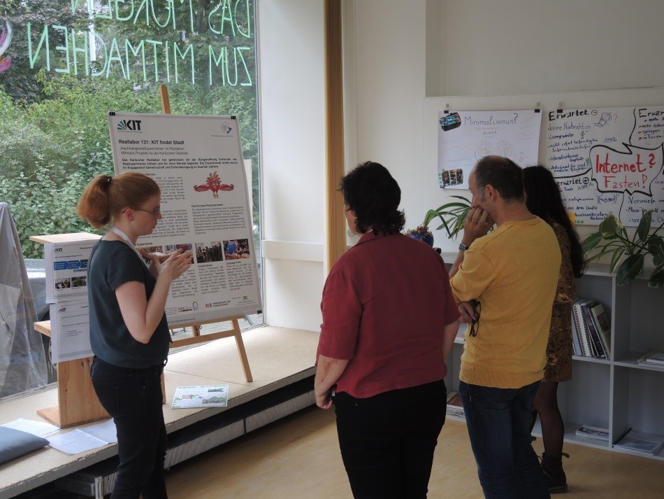 Person erklärt vor Poster am KIT-Projekt mit weiteren Zuhörern in hellem Raum.
