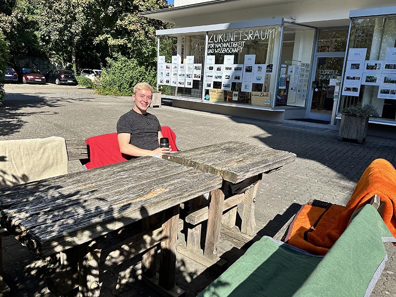 Außenbereich mit rustikalen Holztischen und Stühlen vor dem Zukunftsraum.