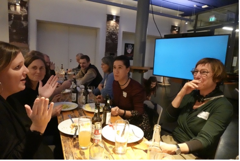 Gruppe Menschen sitzt um einen Tisch beim Essen.