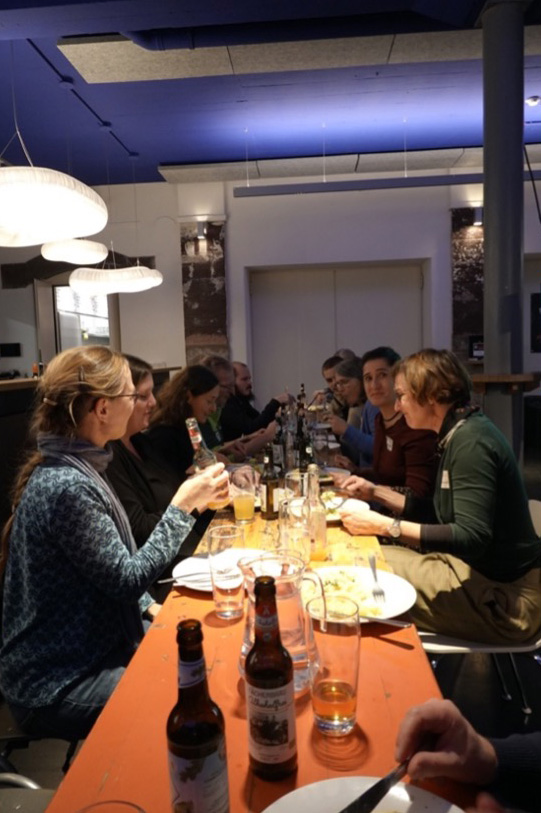 Gruppe von Menschen sitzt an einem langen Tisch mit Essen und Getr&auml;nken darauf.