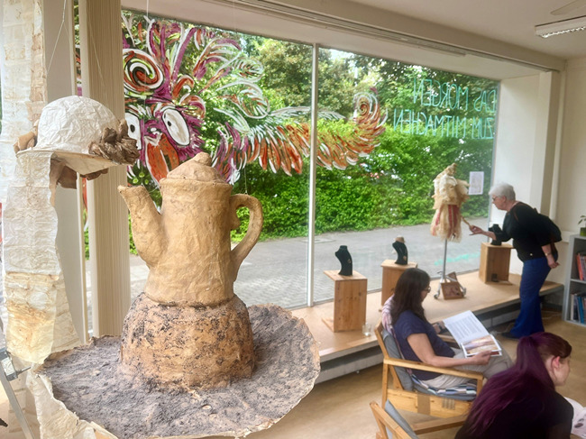 Kunstausstellung mit Skulpturen im Innenraum und einem gro&szlig;en Exponat am Fenster.