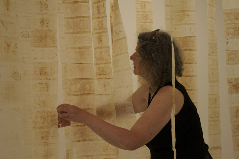 K&uuml;nstlerin arbeitet an h&auml;ngender Stoffbahn in einem Atelier.