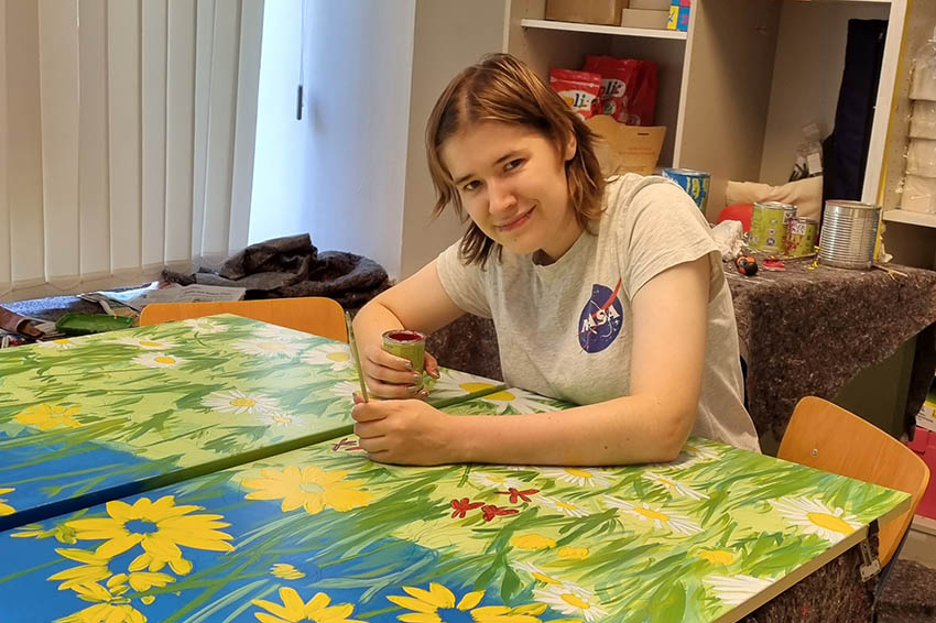 Person bei der Arbeit an einem farbenfrohen Blumenbild.