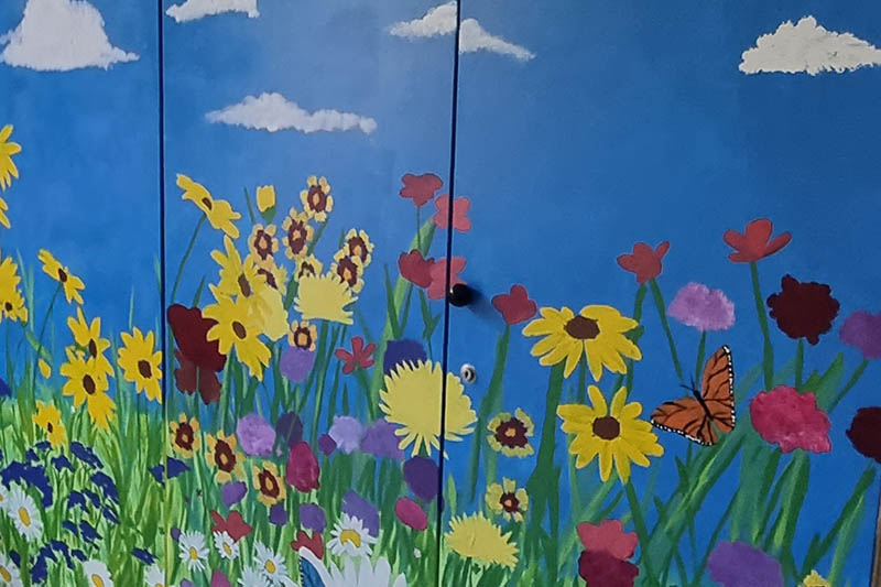 Gem&auml;lde einer bunten Blumenwiese mit Schmetterling unter blauem Himmel mit wei&szlig;en Wolken auf Schrankt&uuml;ren.