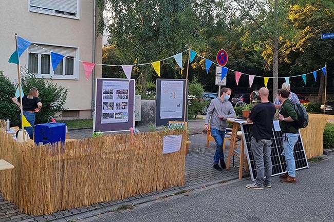 Infostand beim Parking Day auf Parkpl&auml;tzen, Personen unterhalten sich.