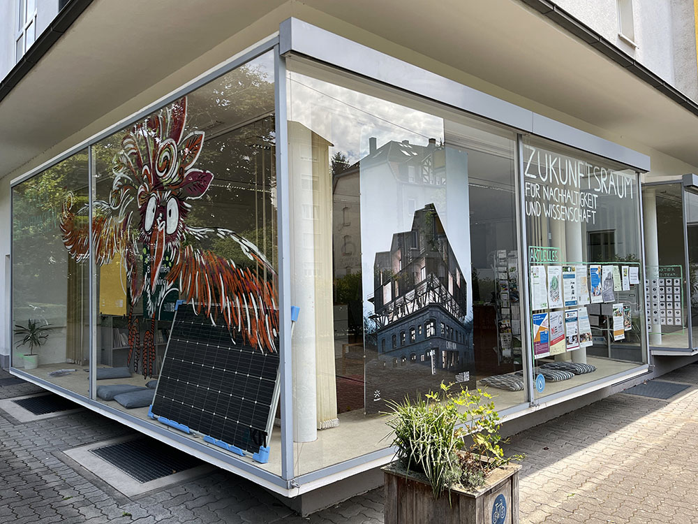 Der Zukunftsraum in Karlsruhe von aussen, an der bunten Glasfassade kleben Poster. 
