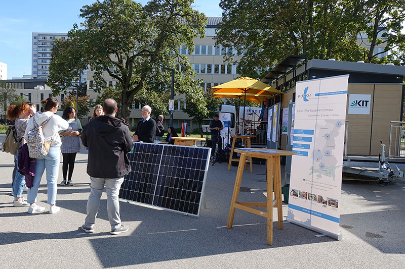 Ein Blakon-Solarmodul steht mit dem MobiLab am Kronenplatz. Viele Menschen stehen darum versammelt und sprechen mit einander